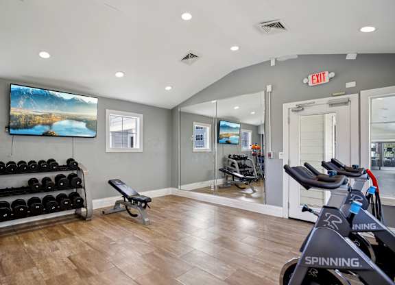 A gym with a row of spinning bikes and a bench with weights.