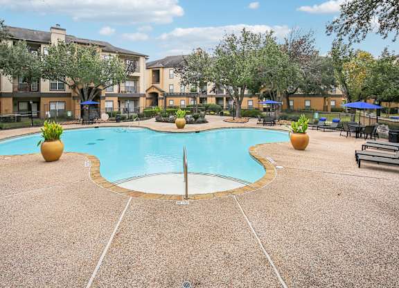 A large swimming pool surrounded by a concrete patio and trees.