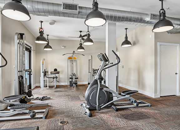 A gym with a variety of equipment including a stationary bike, treadmill, and weights.