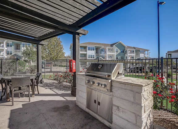 Outdoor grilling station under pergola with patio tables and seating.