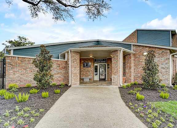 the front of a brick building with a walkway and plants
