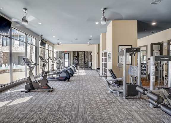 a gym with treadmills and other exercise equipment in a building with large windows