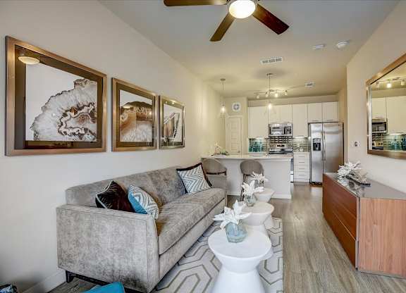 Long living room with plush sofa, pendant lights, and kitchen at the far end.