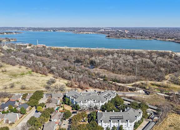 A large house with a grey roof is surrounded by trees and a body of water.