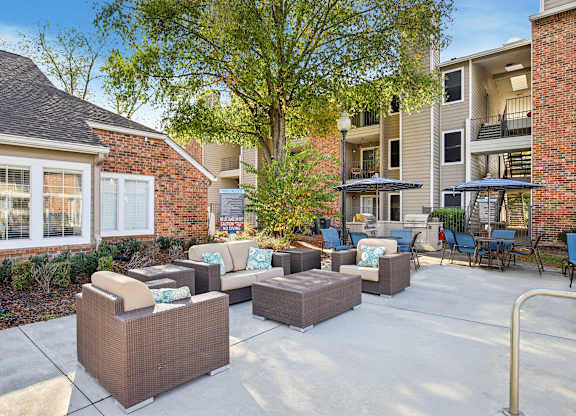 A patio with a couch, chairs, and a table with a tree in the background.
