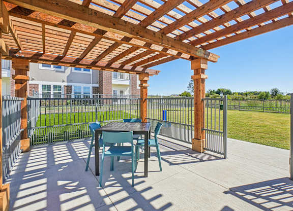 A wooden pergola with a table and chairs is set up on a patio.