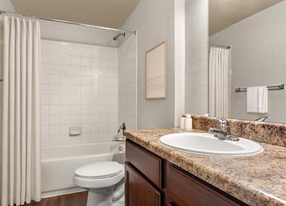 Full bathroom with granite-look counter, undermount sink, and tiled tub surround.