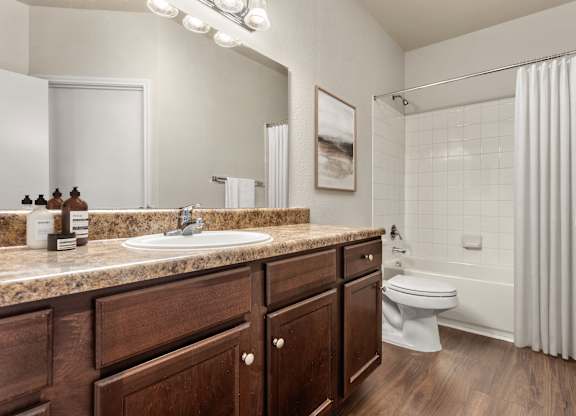 Bathroom vanity with dark wood cabinets, wide mirror, and tub-shower combo.