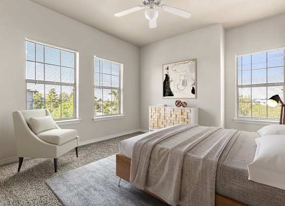 Sunlit bedroom with three large windows, ceiling fan, and cozy sitting chair.
