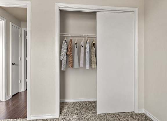 Sliding-door closet with hanging space and adjacent hallway leading to bedroom.
