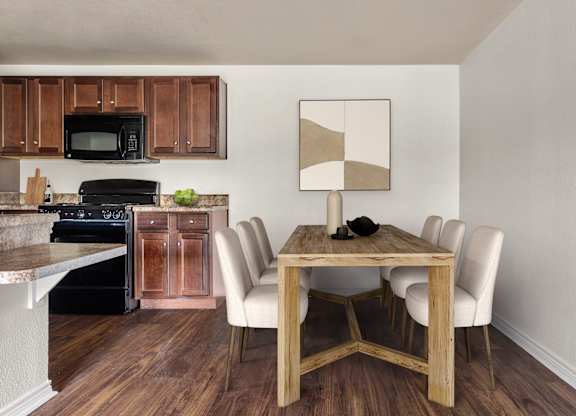 Dining area with six upholstered chairs beside open kitchen with wood-style floors.