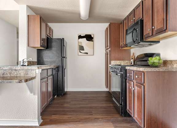 Galley kitchen with espresso cabinets, black appliances, and breakfast bar countertops.