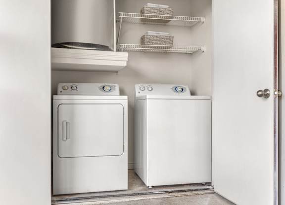 In-home laundry closet with full-size washer and dryer plus wire storage shelves.