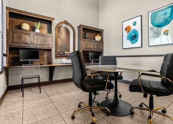 Business center with built-in computer stations and round meeting table with office chairs.