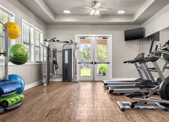 Gym with treadmills, elliptical machines, strength station, and wall-mounted TVs.
