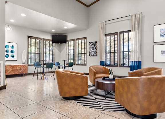 Community lounge with leather chairs, tall windows, and café-style high-top tables.