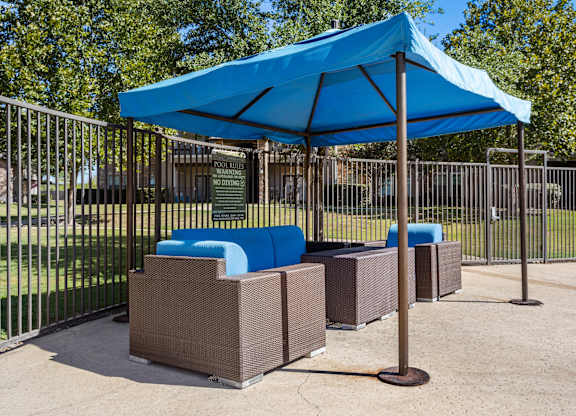 Outdoor lounge seating under blue canopy with cushioned wicker chairs and loveseat.