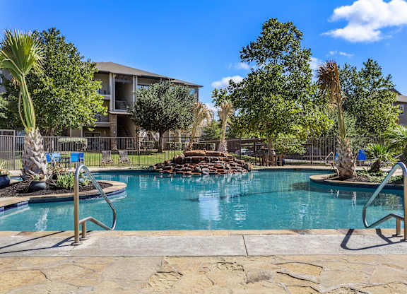 Swimming pool with rock waterfall feature, palm landscaping, and apartment views.