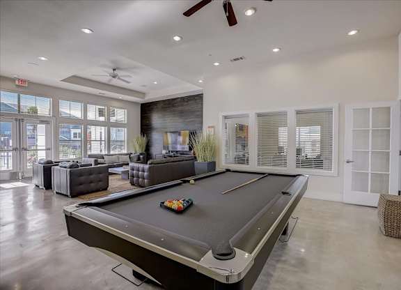 Pool table in clubhouse with lounge seating and oversized windows nearby.