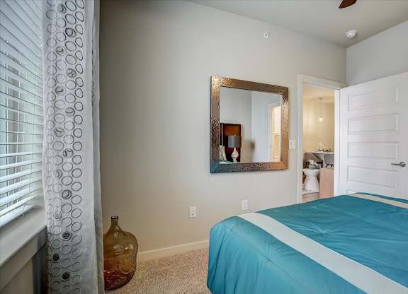 Bedroom corner with wall mirror, soft carpeting, and open door to living space.