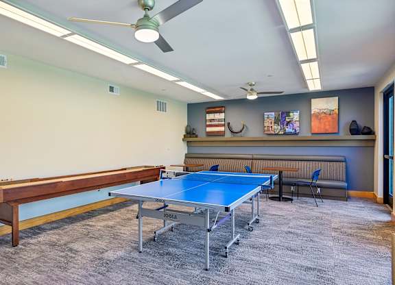 A ping pong table is in the middle of a room with a bench and a fan.