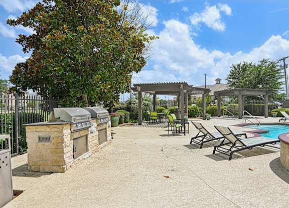 A pool area with a grill and lounge chairs.