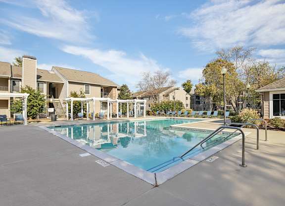 A swimming pool surrounded by a concrete floor and metal railings with a building in the background.