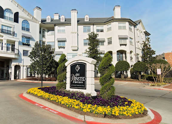 a large white building with a sign in the middle of a roundabout with flowers