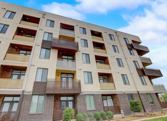 Apartment façade with inset balconies, mixed materials, and trimmed shrubs along the lawn.