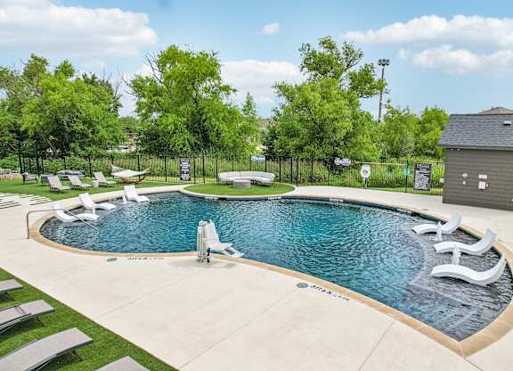 A large outdoor swimming pool surrounded by lounge chairs and trees.