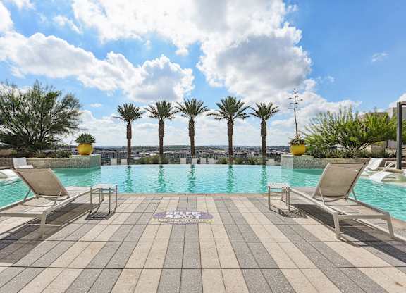 A pool surrounded by palm trees and lounge chairs.