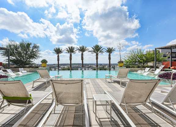A pool surrounded by lounge chairs and palm trees.