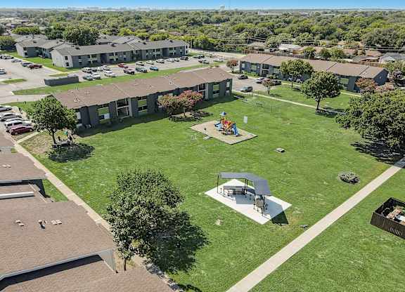 an aerial view of a park with a playground and buildings in the background