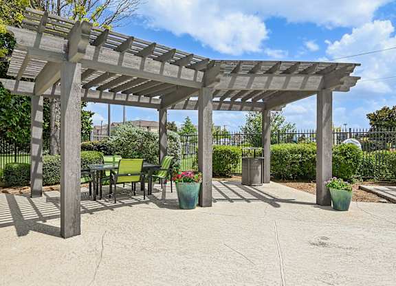 A pergola with chairs and potted plants.
