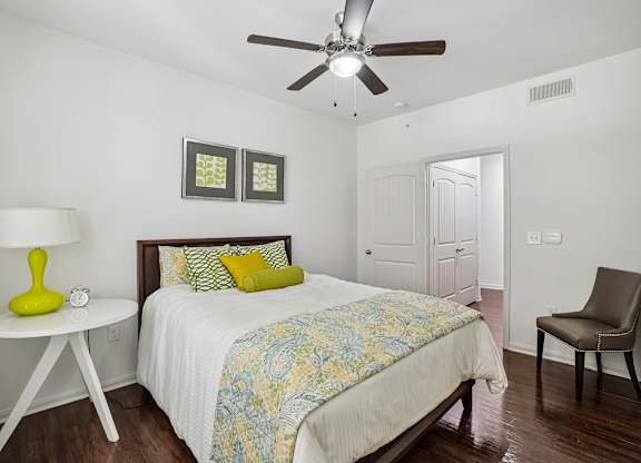 A bedroom with a bed, chair, and ceiling fan.