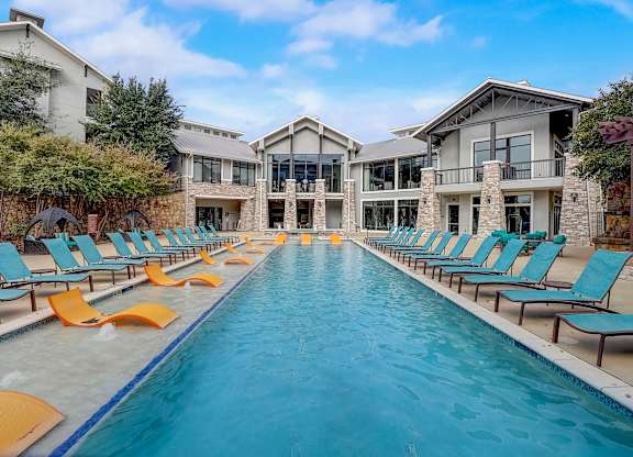 a swimming pool with yellow and blue chairs in front of a house