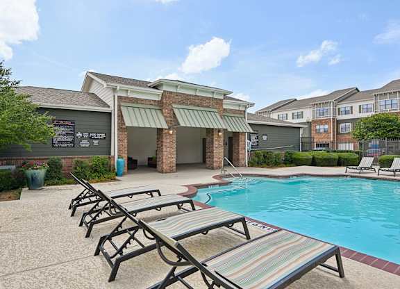 A pool area with sun loungers and a building in the background.