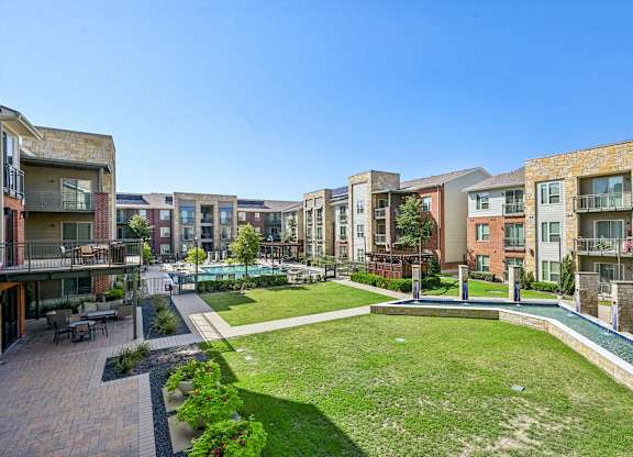 A sunny day at a residential complex with a grassy area and a small pool.