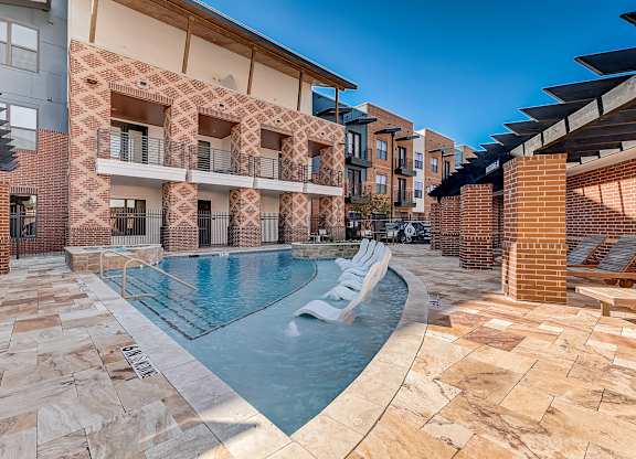 A swimming pool is surrounded by a brick wall and lounge chairs.