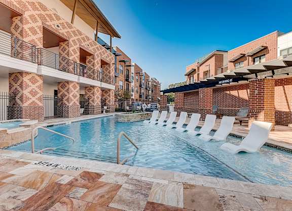 A swimming pool surrounded by white lounge chairs and a brick building.