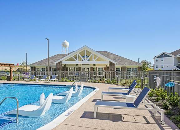 A pool with lounge chairs and a building in the background.