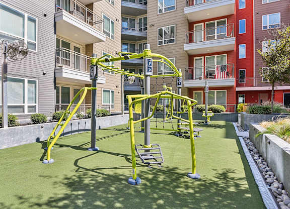 A playground with a yellow swing set in the middle of a grassy area.