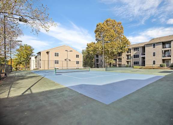A tennis court is surrounded by apartment buildings.
