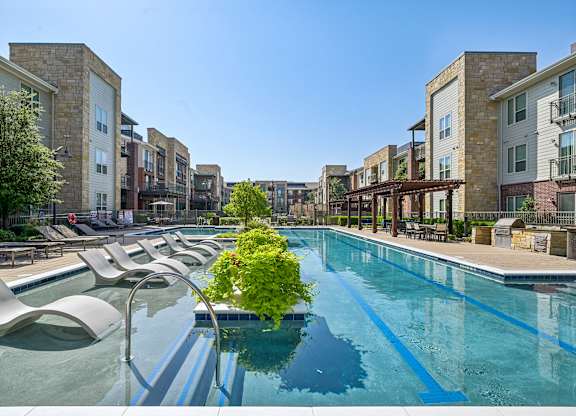 A pool surrounded by lounge chairs and buildings.
