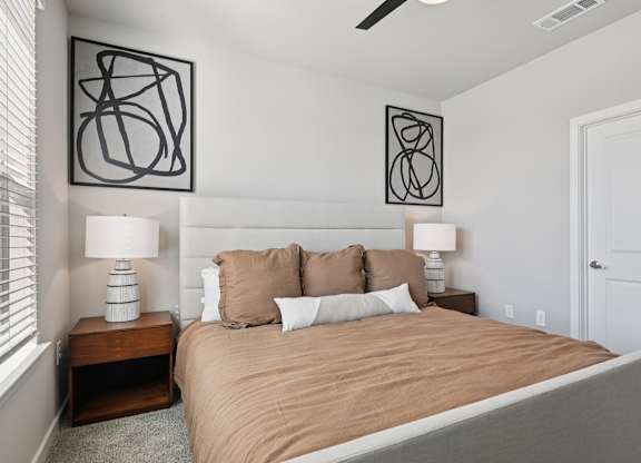 A bedroom with a bed, two lamps, and two wall art pieces.