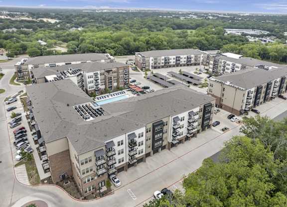 an aerial view of an apartment complex with a parking lot and trees
