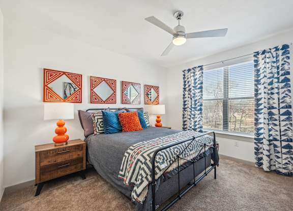 A bedroom with a bed, a ceiling fan, and a window with curtains.