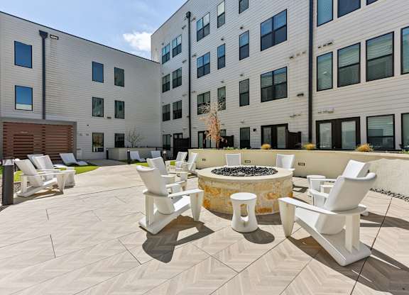 A patio with white chairs and a fire pit in front of a building.