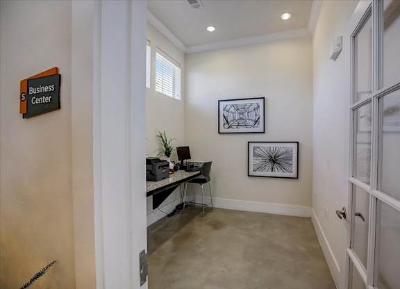 Compact business center room with workstation, glass door, and high windows.
