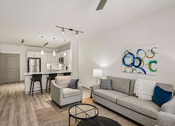 A modern living room with a grey couch, a white coffee table, and a painting on the wall.
